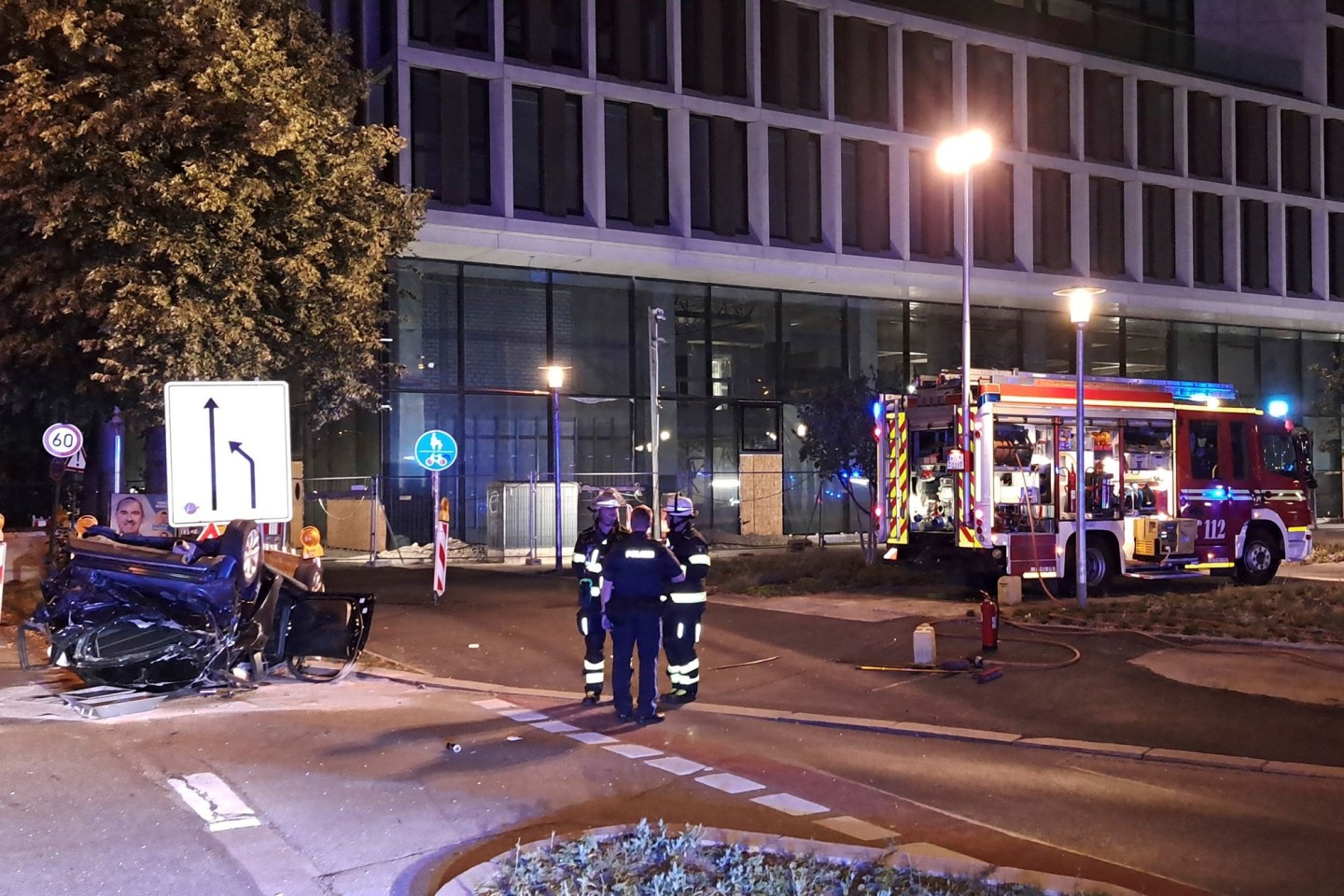 Einsatzkräfte der Feuerwehr und Polizei stehen neben einem zerstörtem Wagen an der Unfallstelle in München.